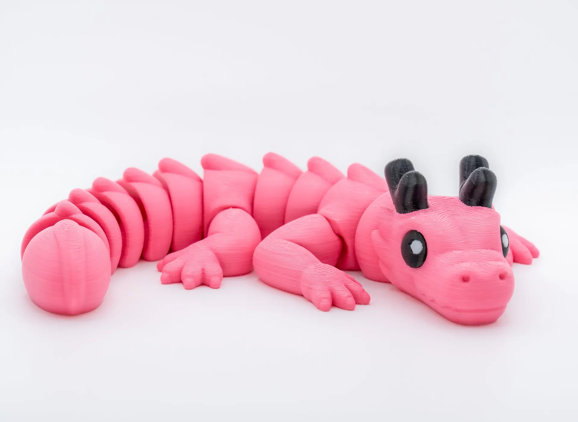 A pink articulated 3D printed dragon lying on a white table